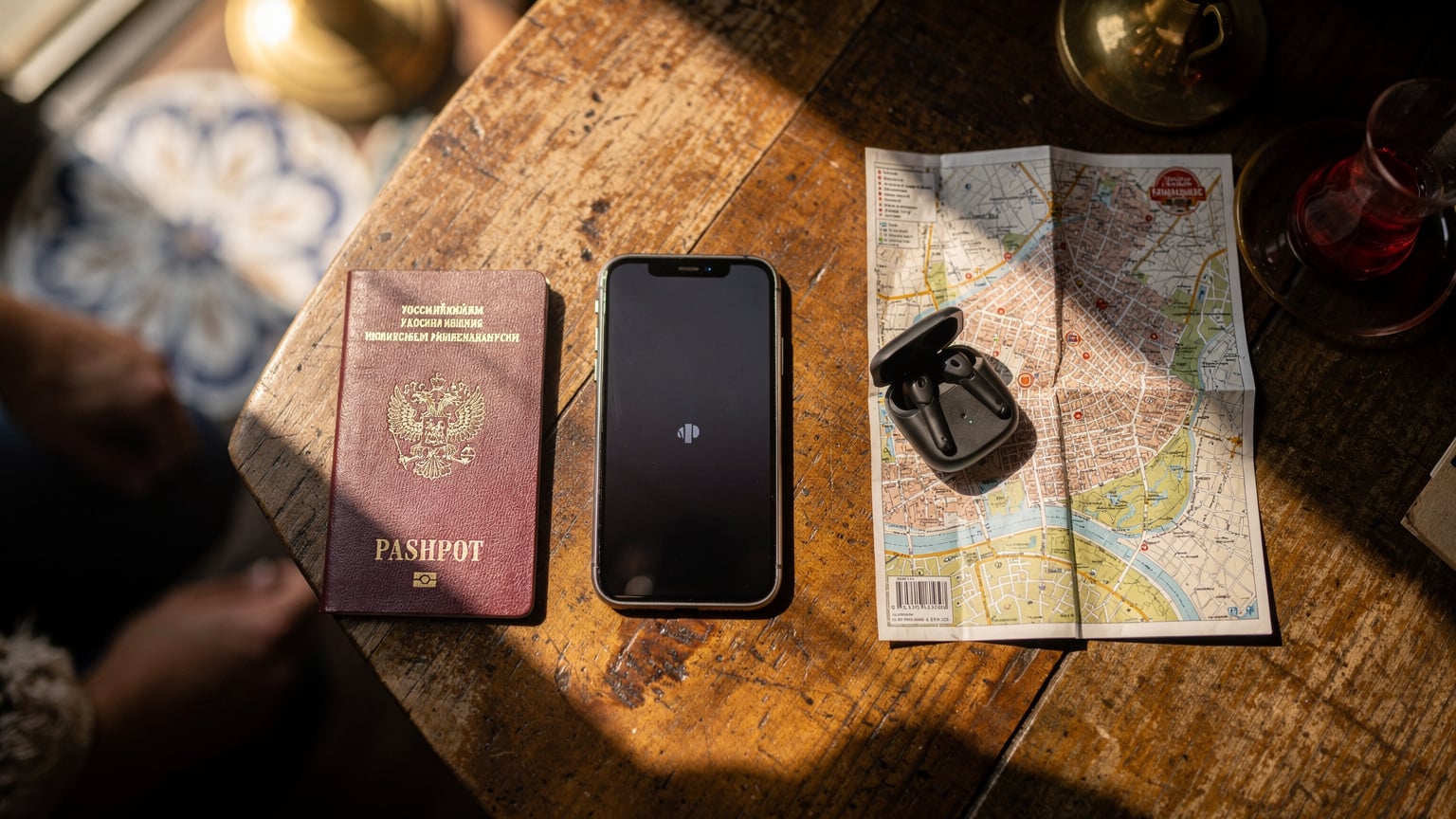 Паспорт, смартфон с активной eSIM, наушники и карта Стамбула аккуратно разложены на деревянном столе в кафе, символизируя готовность к путешествию с современными технологиями.