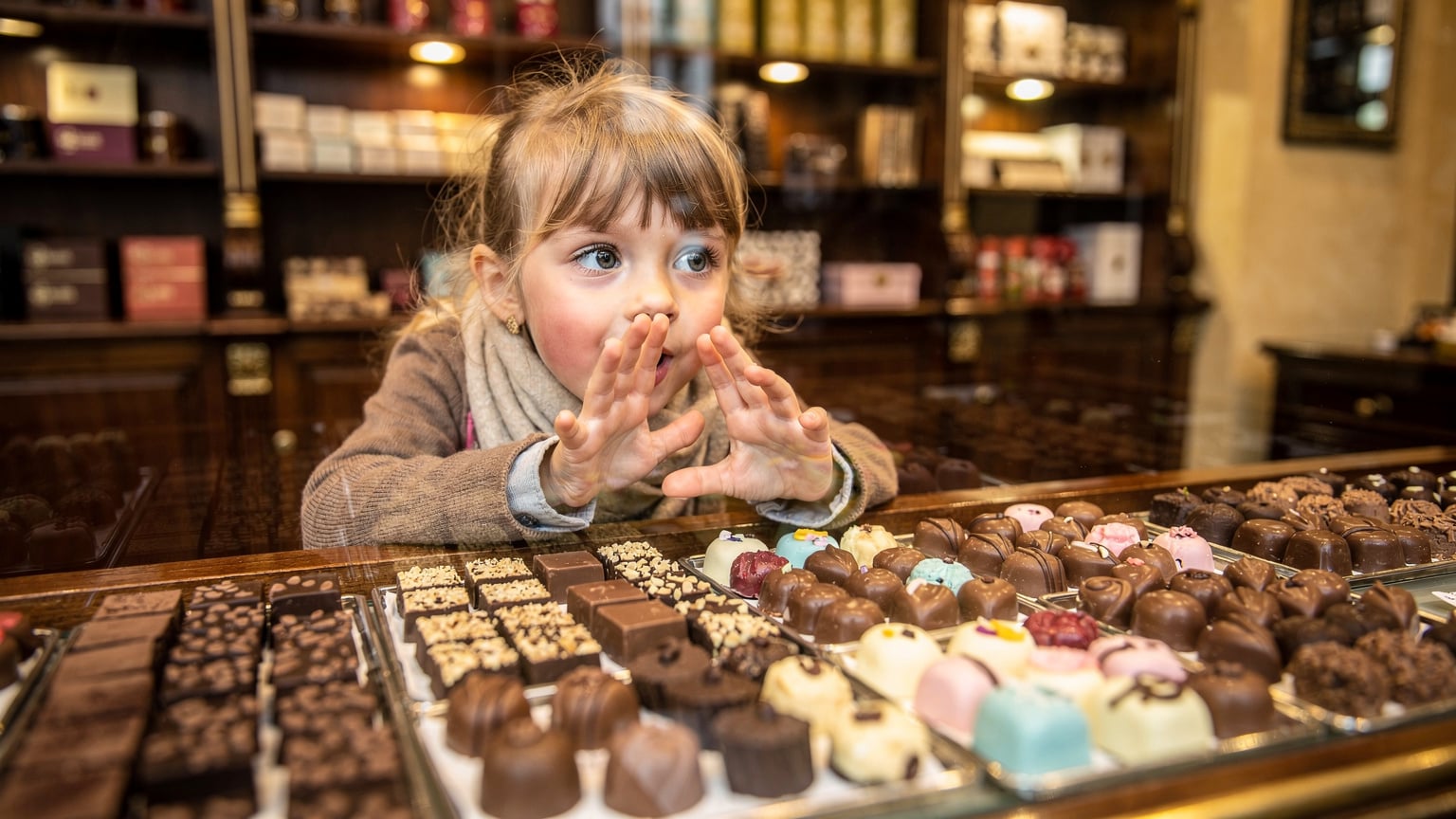 Un bambino di 7 anni con occhi spalancati di fronte a una vetrina colorata di praline in una cioccolateria artigianale a Bruxelles, Belgio.