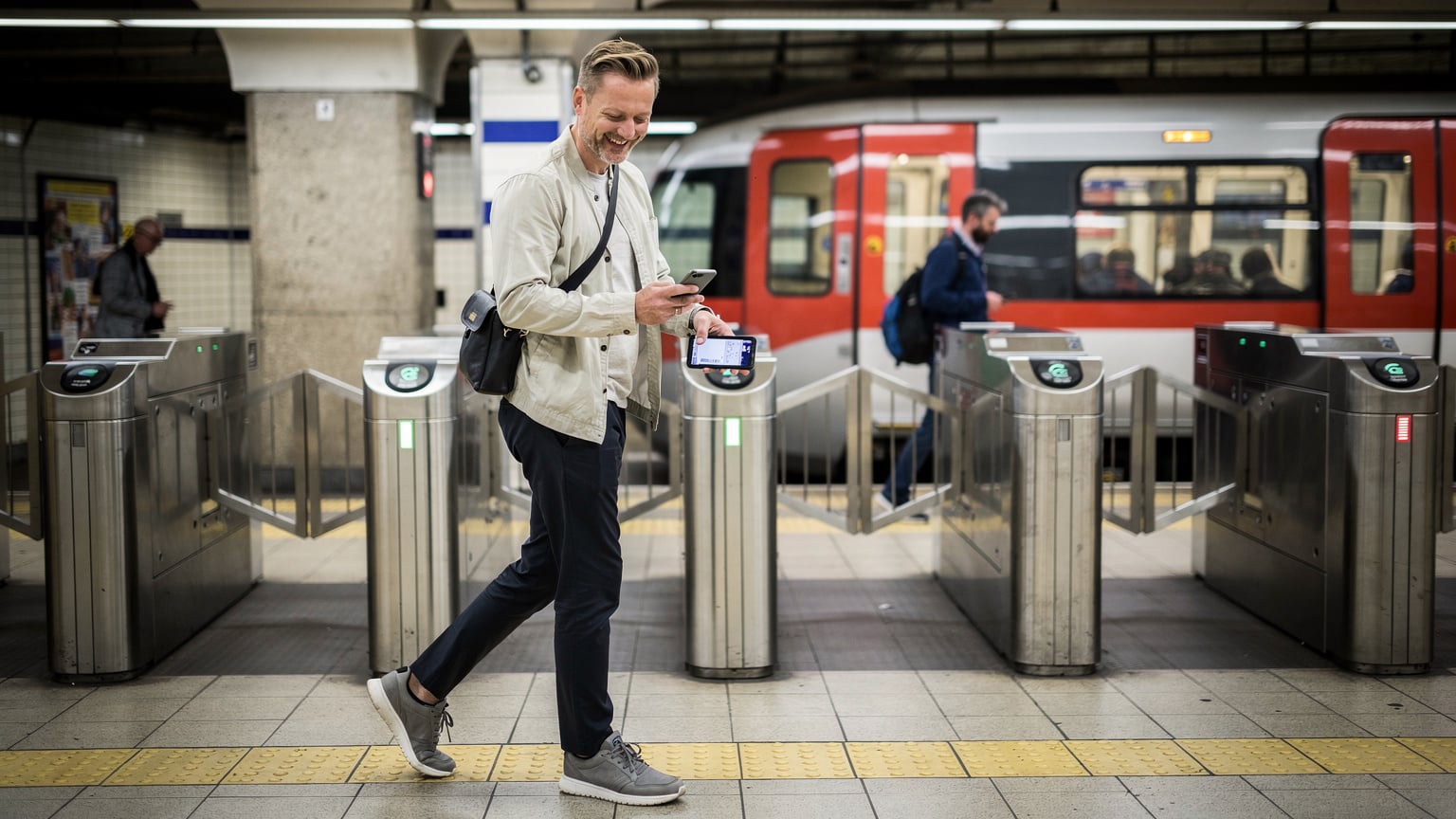 Cestovatel s úsměvem prochází turnikety na stanici metra London Bridge, s telefonem připraveným pro Apple Pay nebo Google Pay.