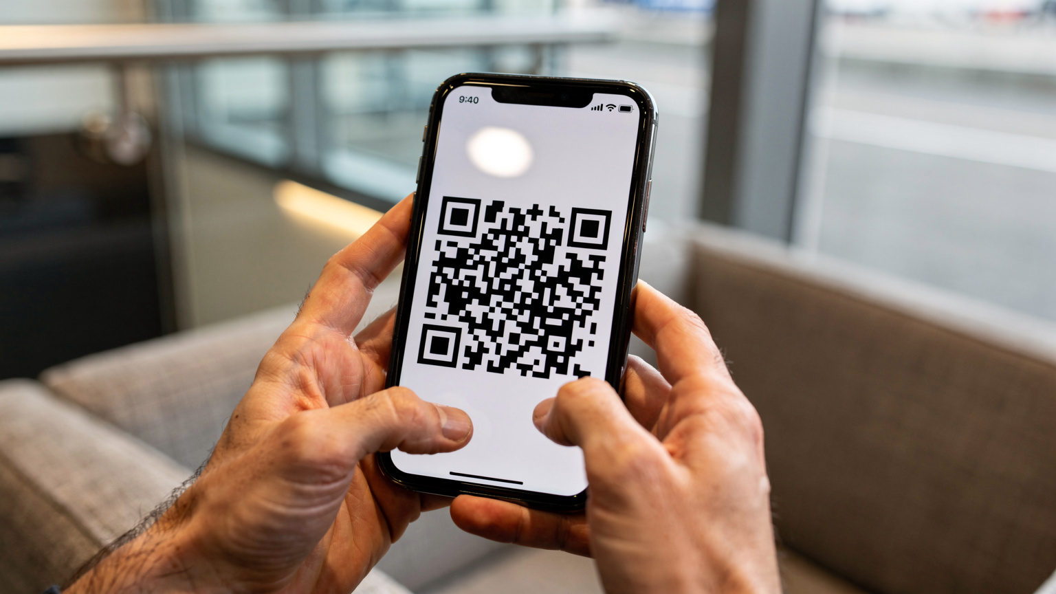 A close-up shot of hands holding a smartphone, with a QR code clearly visible on the screen, ready for eSIM activation, against a blurred background of a modern airport lounge.