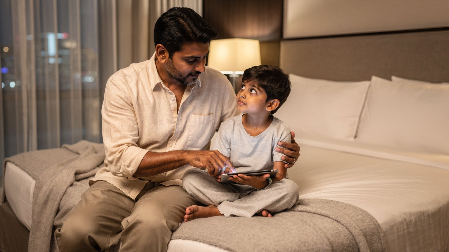 एक पिता अपने बच्चे के टैबलेट पर कुछ सेटिंग एडजस्ट कर रहा है, यह सुनिश्चित करते हुए कि यात्रा के दौरान उसका डेटा उपयोग नियंत्रित रहे और स्क्रीन टाइम सीमित हो.