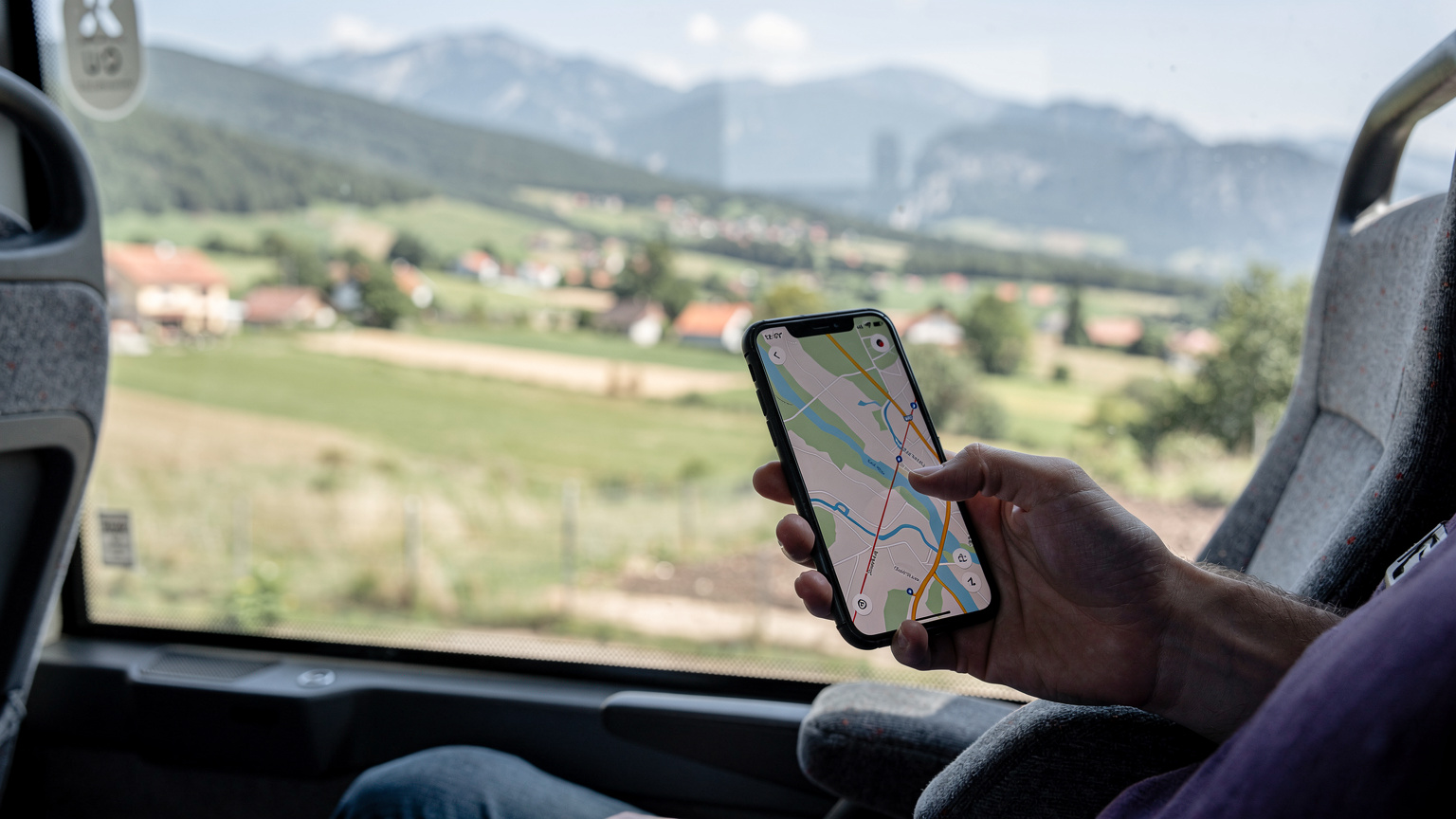 Bosna-Hersek'in yeşil kırsalında seyahat eden bir otobüsün penceresinden dışarıyı seyreden gezginin elinde, açık bir harita uygulaması olan bir telefon.