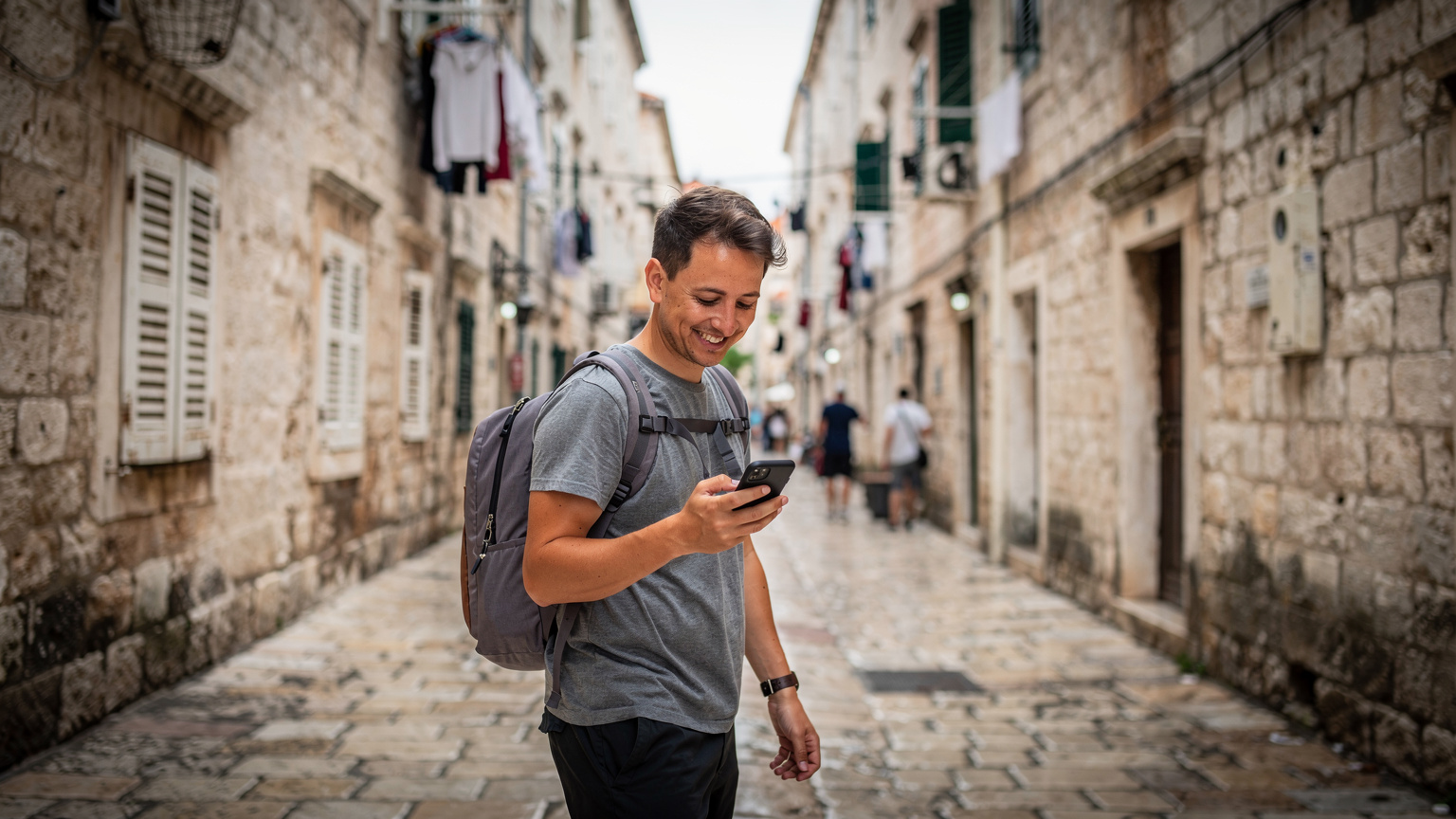 Ein Reisender hält sein Smartphone in der Hand und navigiert durch die engen Gassen der Altstadt von Split, Kroatien, während er gleichzeitig die historischen Gebäude und die lebhafte Atmosphäre genießt.