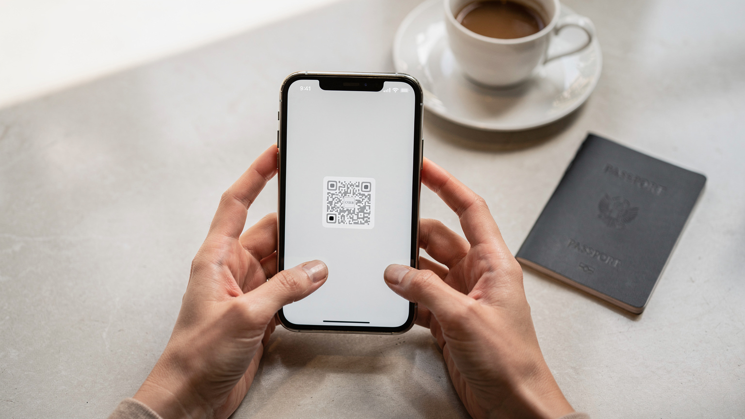 Tangan seorang wanita sedang memegang ponsel, menampilkan layar yang menunjukkan proses aktivasi eSIM dengan kode QR yang siap dipindai, di atas meja kafe yang rapi dengan secangkir kopi dan paspor di latar belakang.