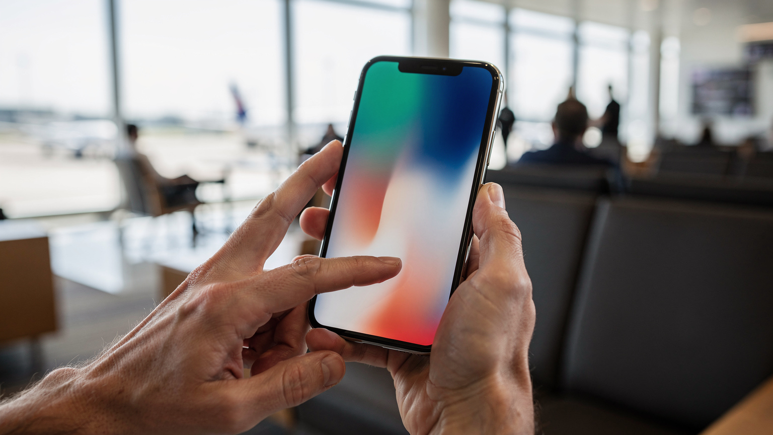 Un primo piano delle mani di una persona che tiene uno smartphone e scorre il dito sullo schermo per attivare un profilo eSIM, con lo sfondo sfocato di un lounge aeroportuale internazionale.