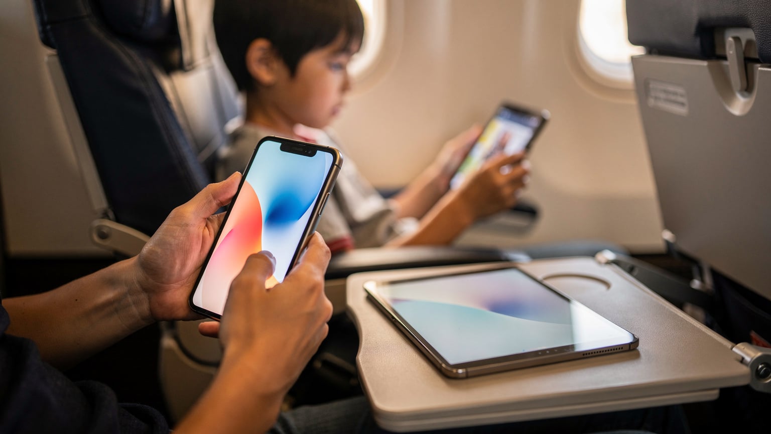 日本からハワイへの飛行機内で、子供がiPadでダウンロード済みの映画を見ている様子。親は自分のスマホでCellesimアプリを開き、現地でのeSIM準備状況を最終確認している。