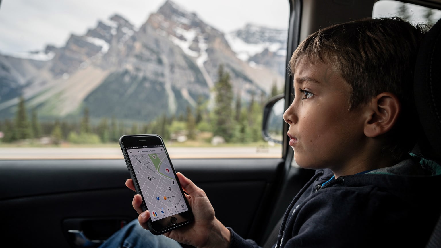 Un téléphone affichant une carte hors ligne pendant un road trip au Canada, avec un enfant qui regarde par la fenêtre, fasciné par le paysage.