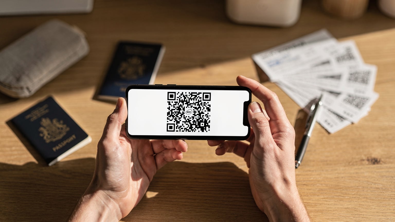 Des mains tenant un smartphone affichant un QR code d'activation eSIM, avec en arrière-plan flou, des passeports et des billets d'avion, symbolisant la préparation d'un voyage au Canada.