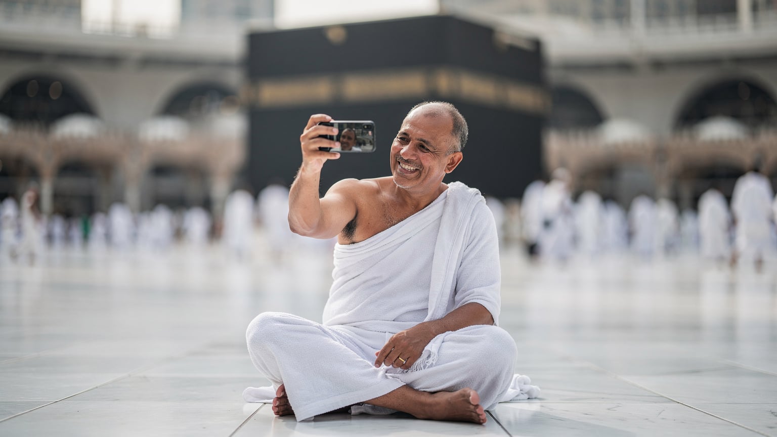 Seorang jemaah haji sedang membuat panggilan video kepada ahli keluarga menggunakan aplikasi WhatsApp sambil duduk di kawasan dataran Masjidil Haram.