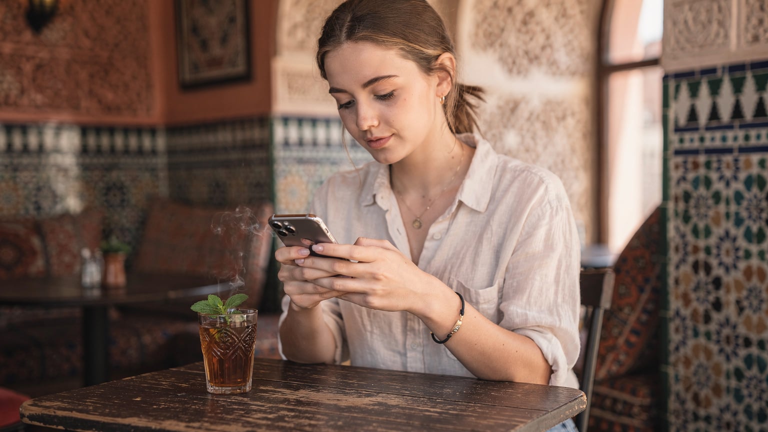 Kobieta w marokańskiej kafejce, przeglądająca telefon z widocznym ekranem ustawień eSIM, obok szklanka herbaty.