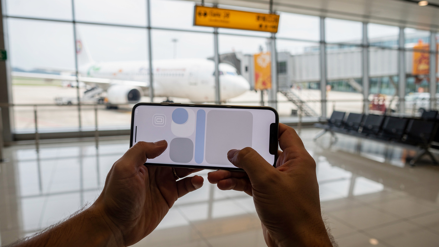 一位旅客在香港國際機場的登機口,手持一部港版iPhone,屏幕上顯示eSIM激活流程,背景是飛機和登機橋。