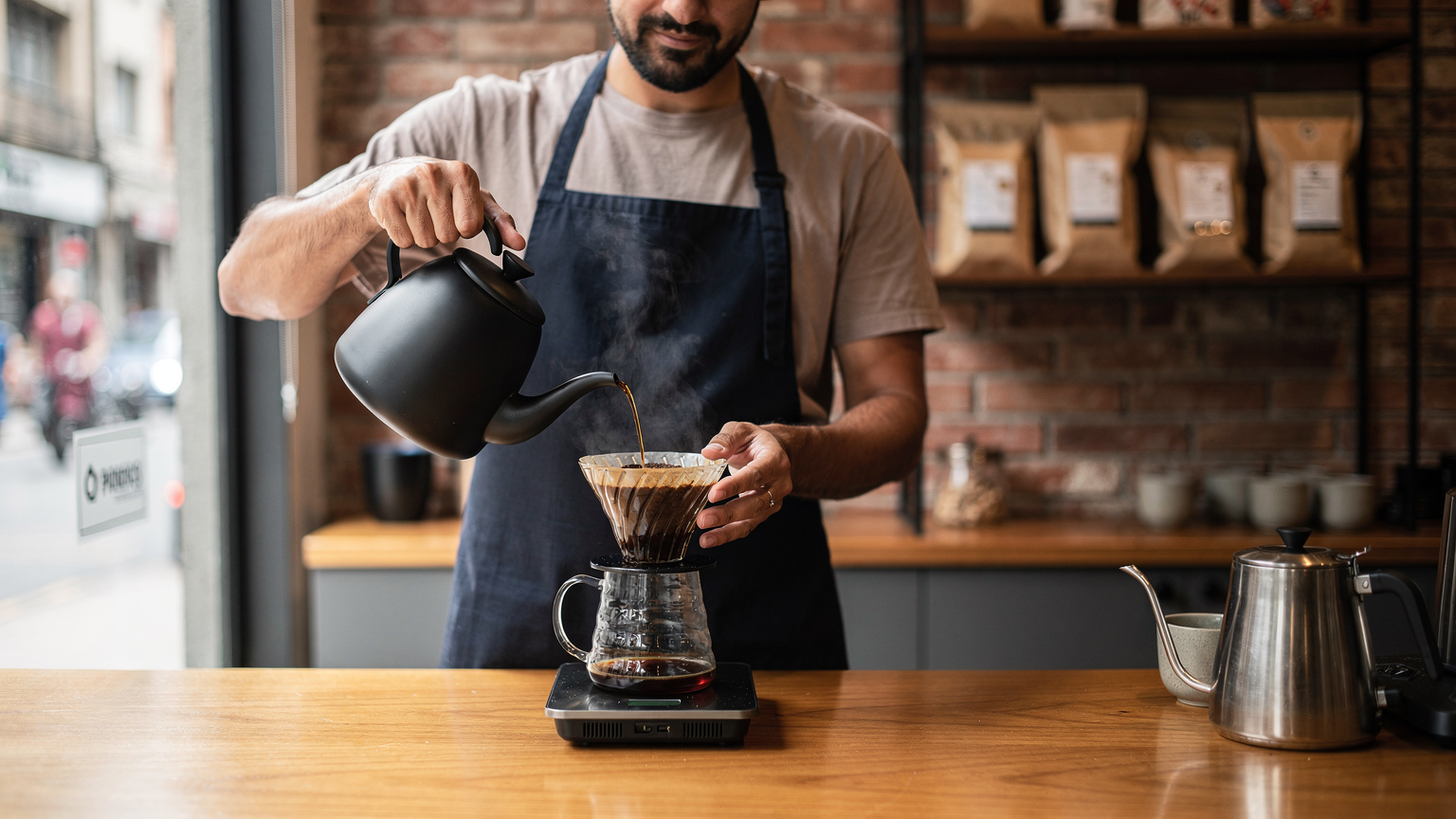Un barista experimentado prepara un café en una moderna cafetería del barrio de Pinheiros, São Paulo, con granos tostados en exhibición al fondo.