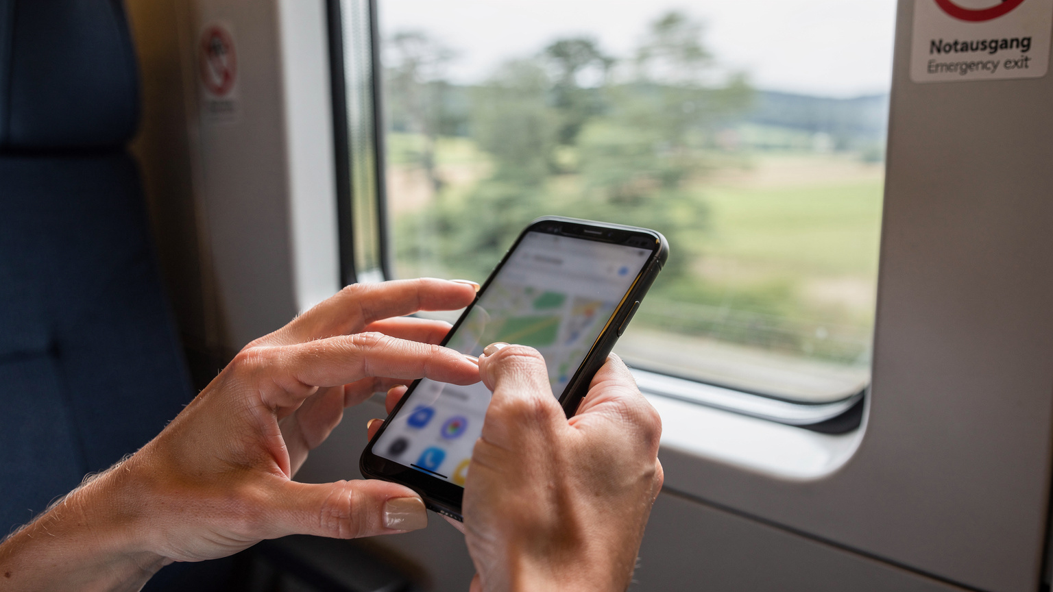 Manos de un viajero deslizando el dedo por la pantalla de un smartphone, configurando las opciones de datos en segundo plano para una aplicación de mapas en un tren europeo.