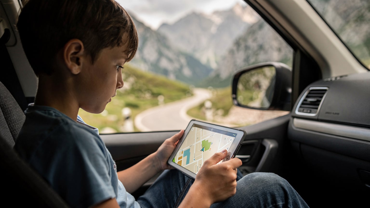 Ein Kind mit einem Tablet auf dem Rücksitz eines Autos, das durch die montenegrinische Landschaft fährt.