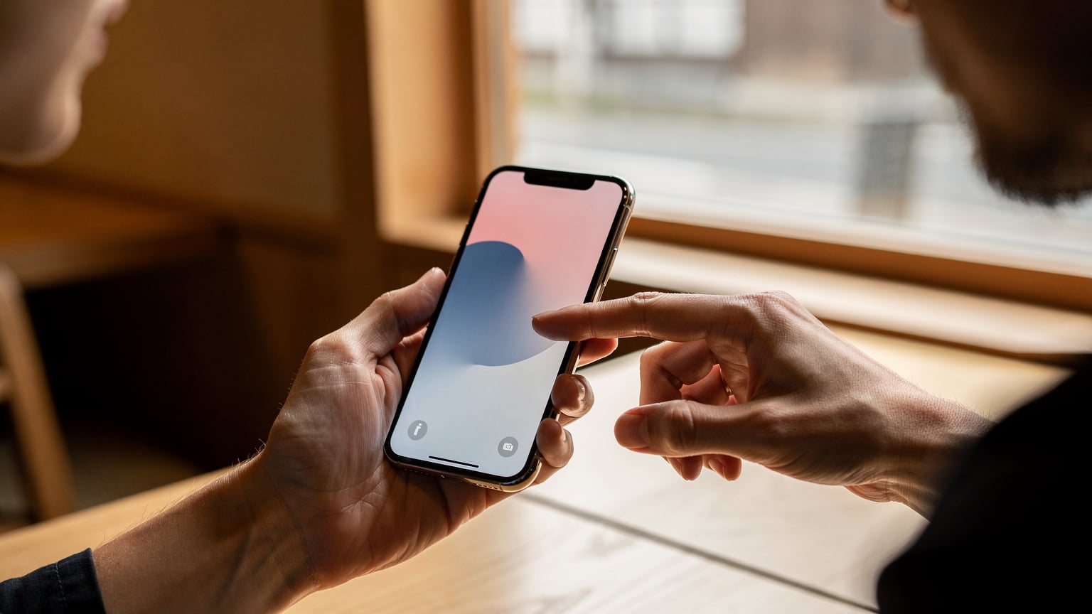 Close-up of human hands, one holding a smartphone displaying a loading screen or an eSIM activation prompt, the other hand poised over the screen, in a well-lit cafe in Kyoto, Japan.