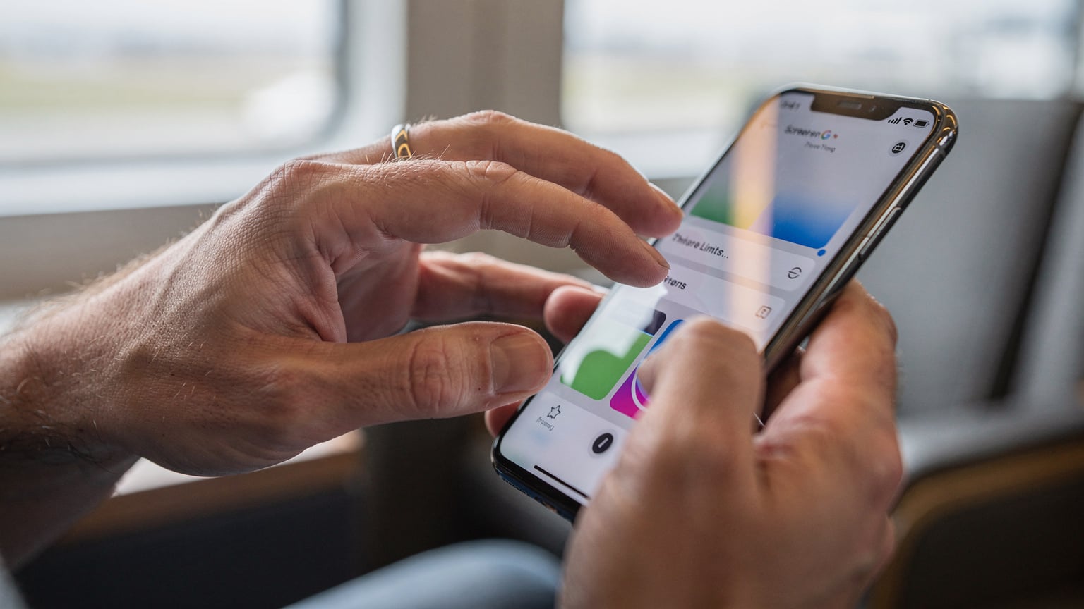 Mãos de um pai ou mãe configurando as opções de Tempo de Uso no iPhone, com foco nas configurações de dados móveis e limites de aplicações, em segundo plano, um cenário de viagem desfocado.