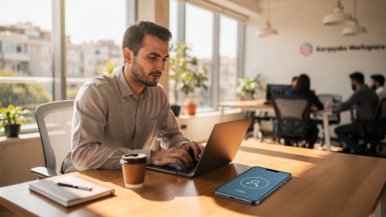 Eine Person sitzt an einem Tisch in einem sonnigen Co-Working-Space in Izmir, arbeitet an einem Laptop und hat ein Smartphone mit aktivem eSIM-Signal daneben liegen.