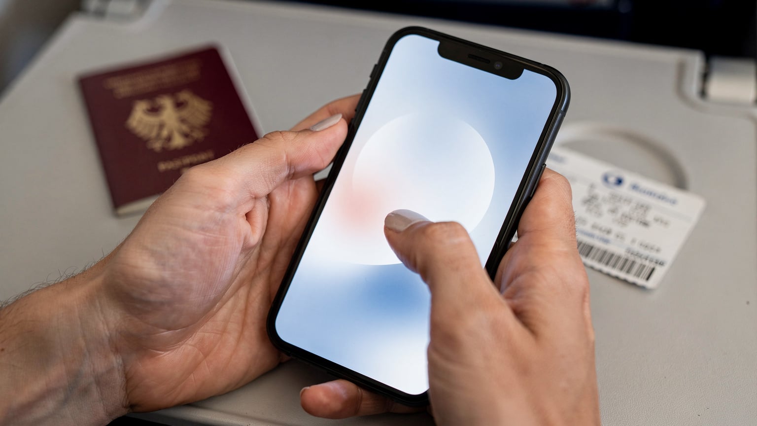 Nahaufnahme der Hände eines Reisenden, der ein Smartphone hält und auf dem Bildschirm eine eSIM-Installationsanleitung verfolgt, mit einem halb verdeckten Reisepass im Hintergrund.