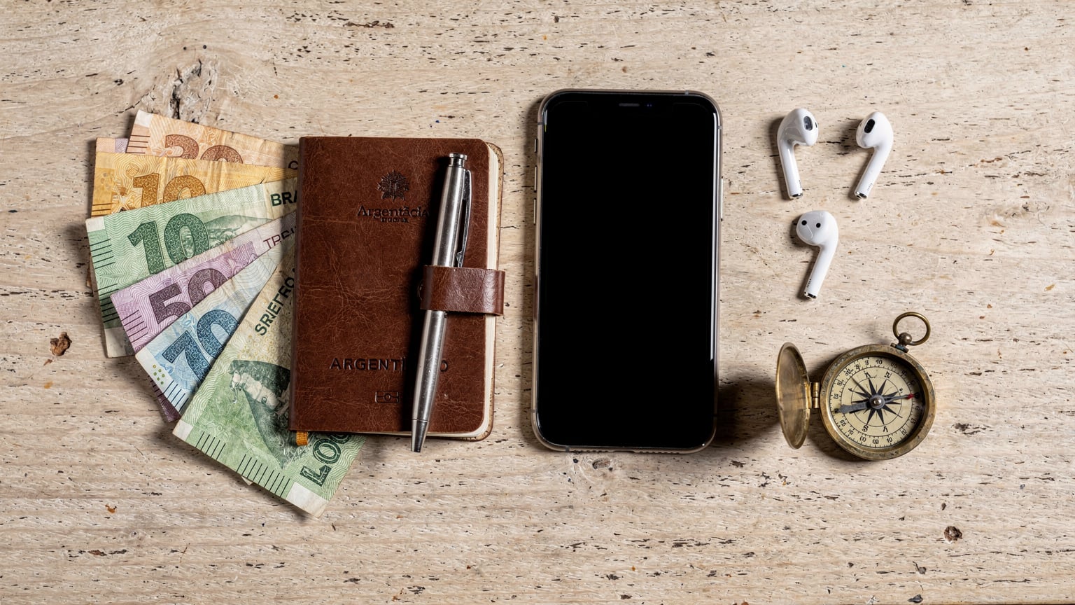 An overhead flat-lay shot of travel essentials, including a passport, an iPhone with an eSIM plan visible, local currency, and a small journal, representing organized travel.