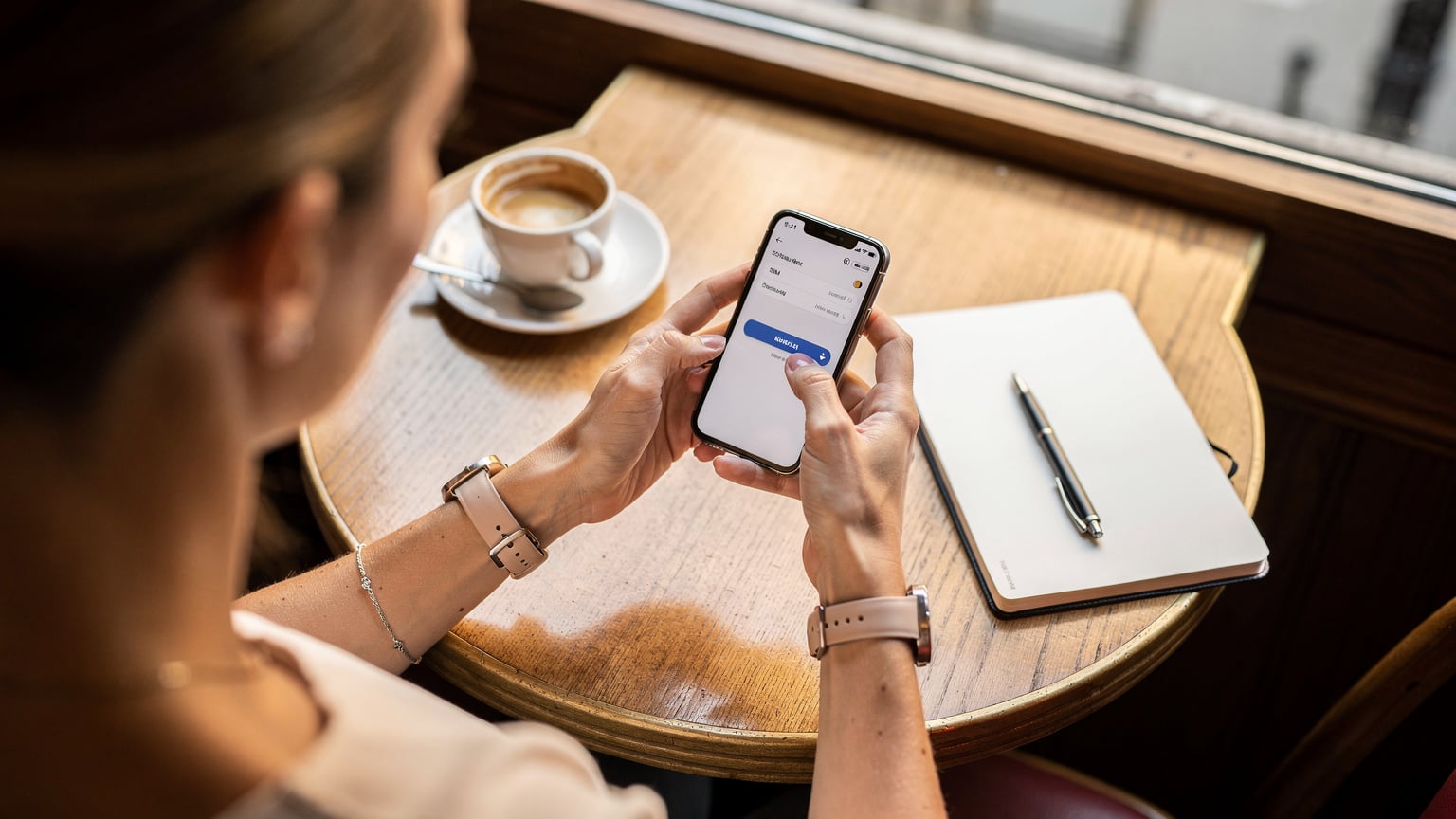 Bir seyahat bloggerı, Paris'teki bir kafede, rahat bir öğleden sonra kahvesi eşliğinde telefonunda eSIM ayarlarını yapıyor. Eli ekranda, titizlikle seçenekleri gözden geçiriyor.