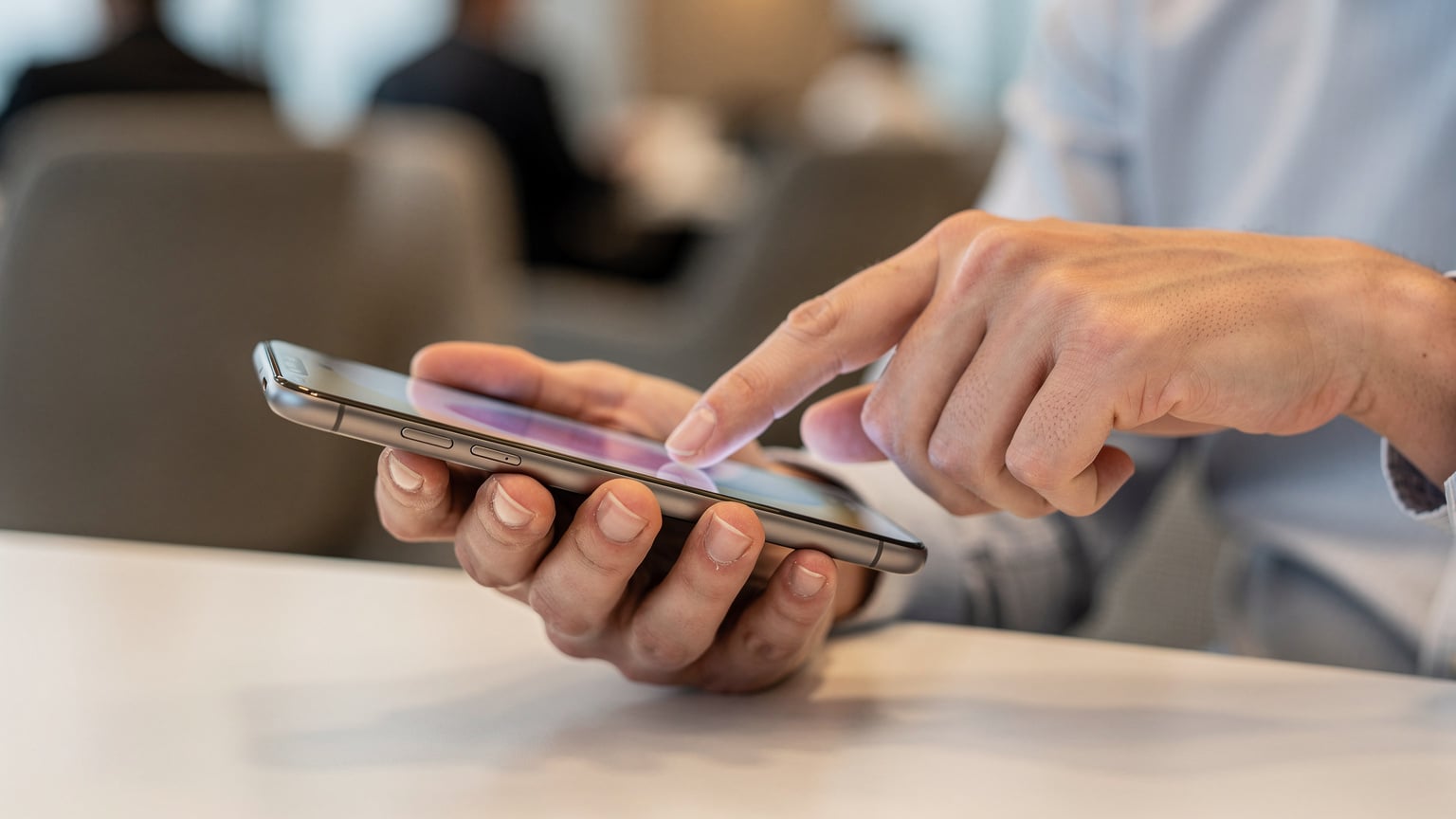 空港ラウンジで、ビジネスパーソンの手がスマートフォンを持ち、eSIMのQRコードをスキャンして設定を行っているクローズアップ。指先が画面に触れている。