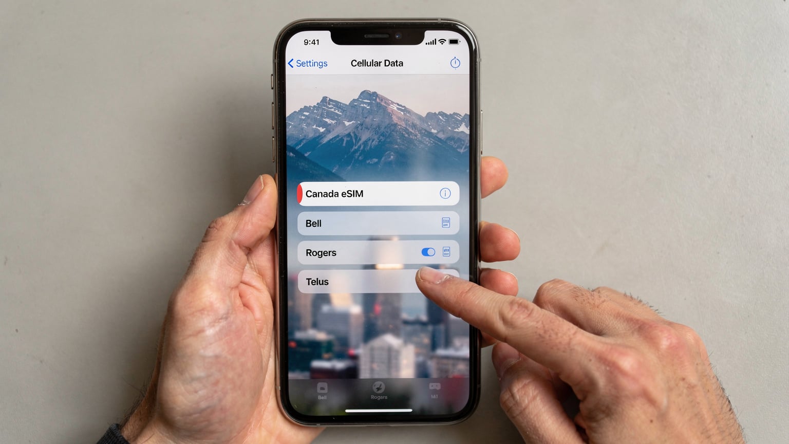Un smartphone avec l'application de gestion d'eSIM ouverte, montrant un profil eSIM "Canada" actif et la sélection manuelle des réseaux Bell, Rogers et Telus, avec des paysages variés du Canada sur l'écran d'accueil.