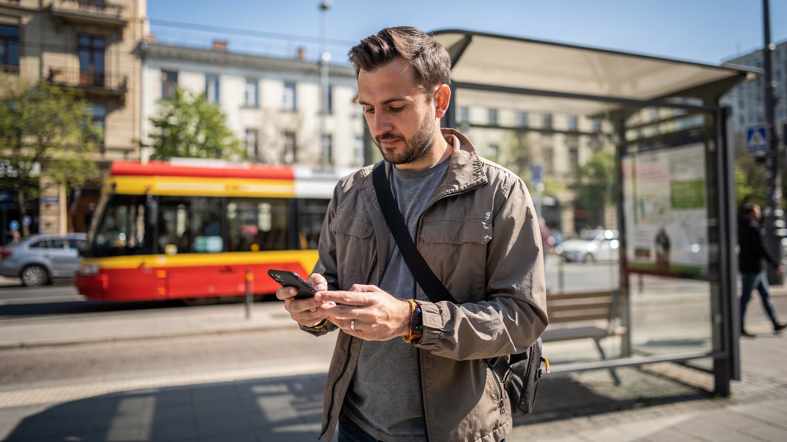 Een reiziger kijkt op hun telefoon naar de route voor het openbaar vervoer in Warschau, Polen, met trams op de achtergrond.