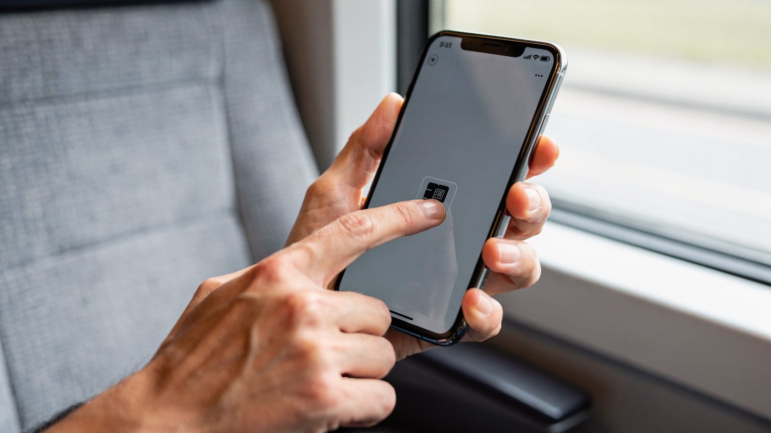 Eine Nahaufnahme zeigt die Hand einer Person, die auf einem Smartphone-Bildschirm die Aktivierung eines neuen eSIM-Profils bestätigt, mit dem ICE-Interieur im leicht unscharfen Hintergrund.