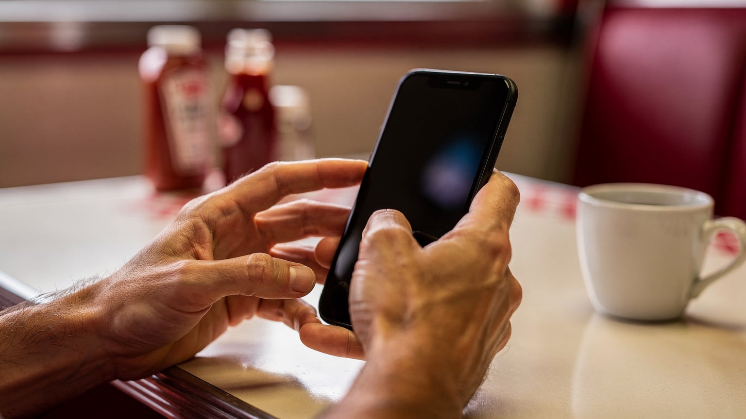 A close-up of a traveler's hands carefully checking data usage settings on a smartphone, with a blurred backdrop of a typical American roadside diner table, suggesting a moment of planning during a road trip.