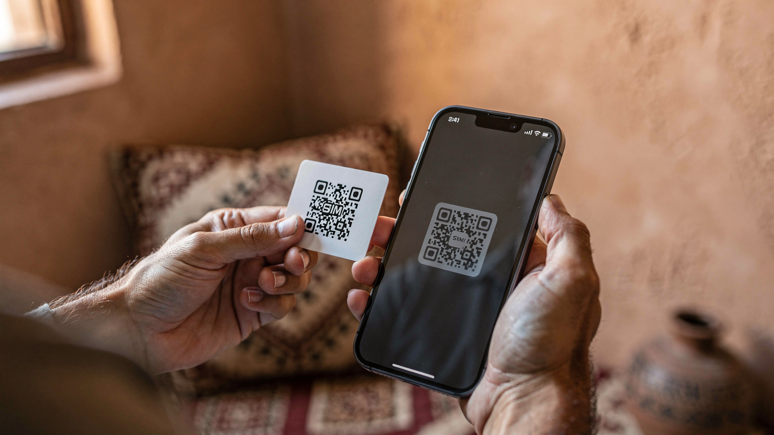 Zbliżenie na dłonie podróżnika aktywującego eSIM na smartfonie, z ekranem pokazującym proces skanowania kodu QR, na tle minimalistycznego wnętrza riadu.