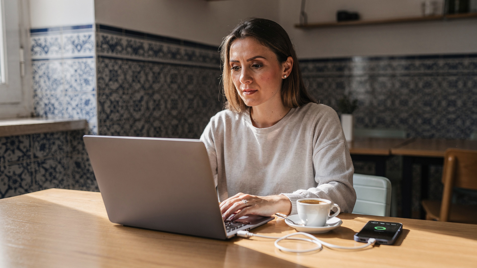 Digitální nomádka pracuje na svém notebooku v co-workingovém prostoru v historické čtvrti Alfama v Lisabonu, s telefonem vedle pro hotspot.