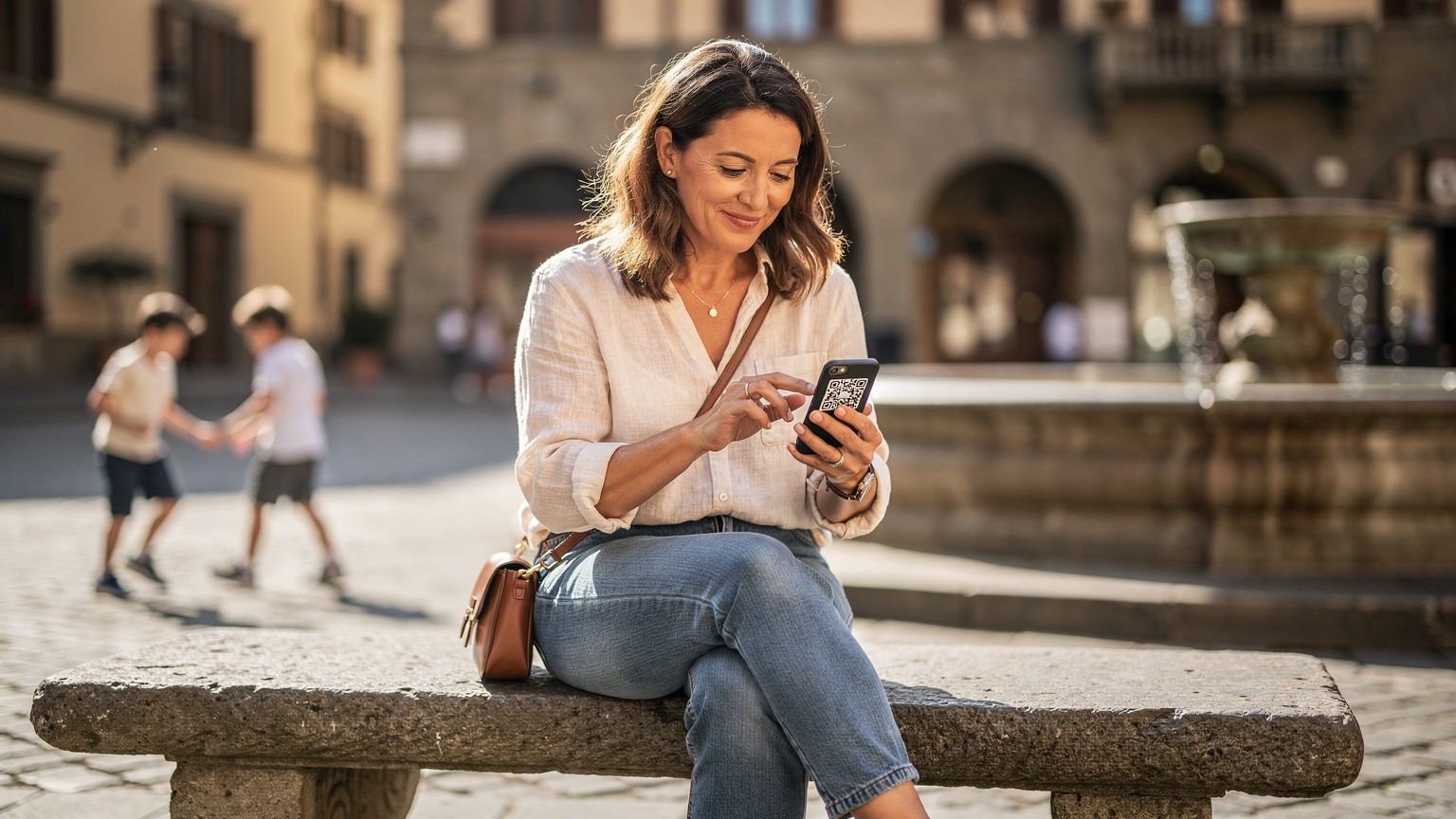 A mother, mid-30s, with a relaxed smile, sitting on a park bench in a sunny piazza in Florence, Italy, gently tapping her smartphone to set up a Cellesim eSIM. Her two children, aged 7 and 9, are playing with a small ball nearby, partially visible in the background, out of focus.