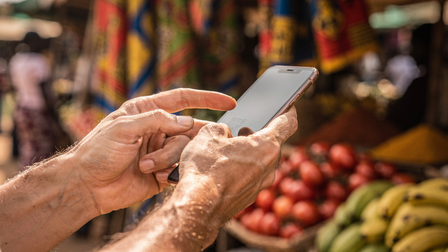 A close-up of a traveler's hands, worn from adventure, interacting with their smartphone to scan a Cellesim eSIM QR code, set against a blurred backdrop of a traditional Tanzanian market scene.