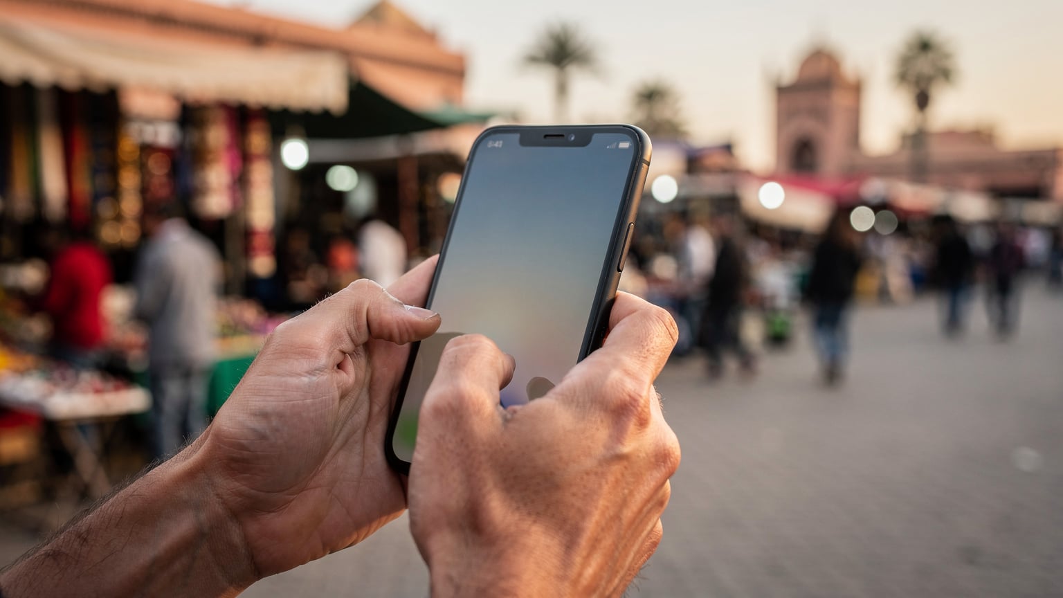 Close-up of a person's hands holding a smartphone, with a WhatsApp chat open, showing text messages quickly sending and receiving in a busy marketplace in Marrakech, Morocco.