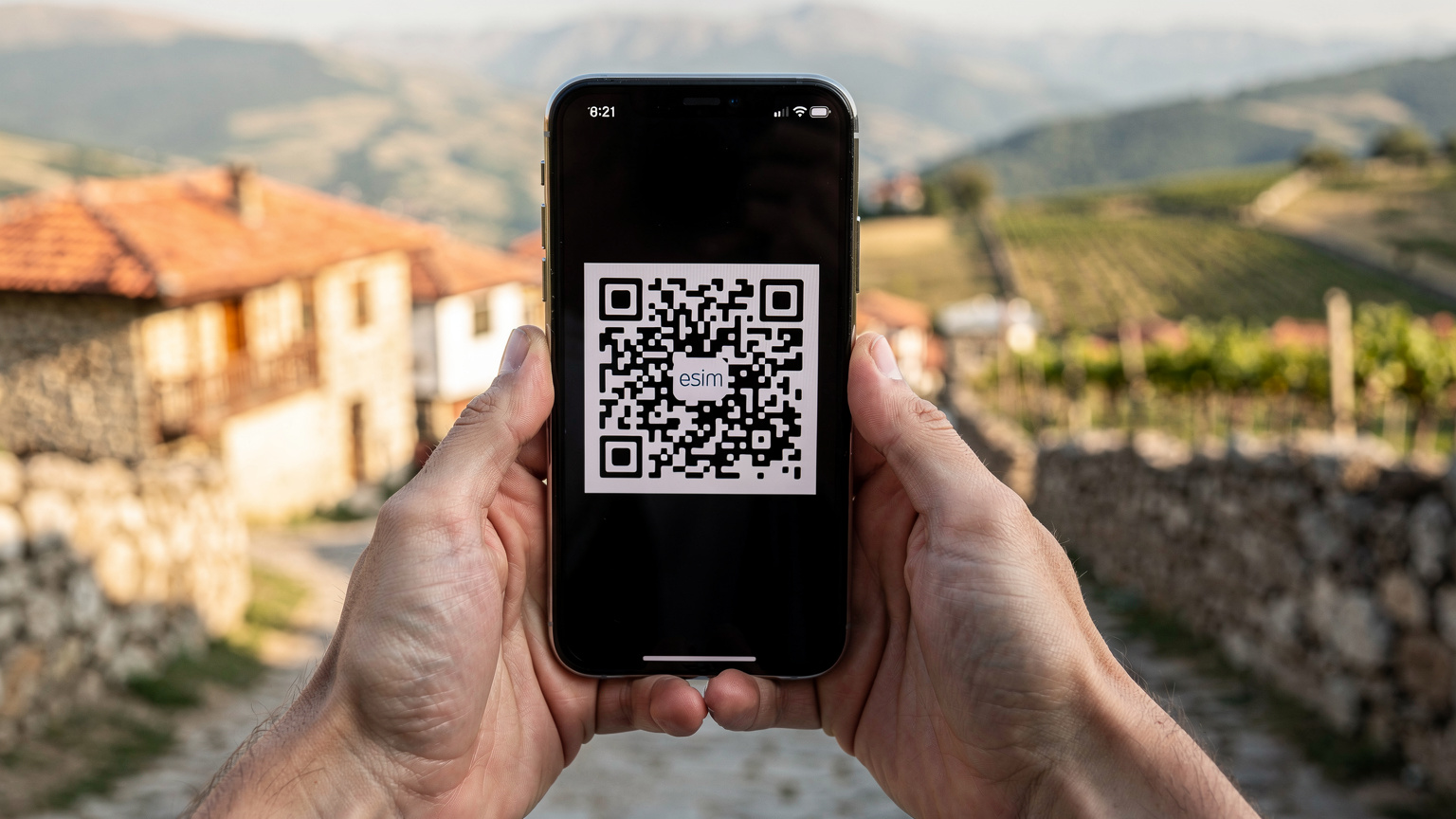 Крупный план рук, держащих смартфон, на экране которого показан QR-код для активации eSIM, на фоне размытого пейзажа грузинской деревни.