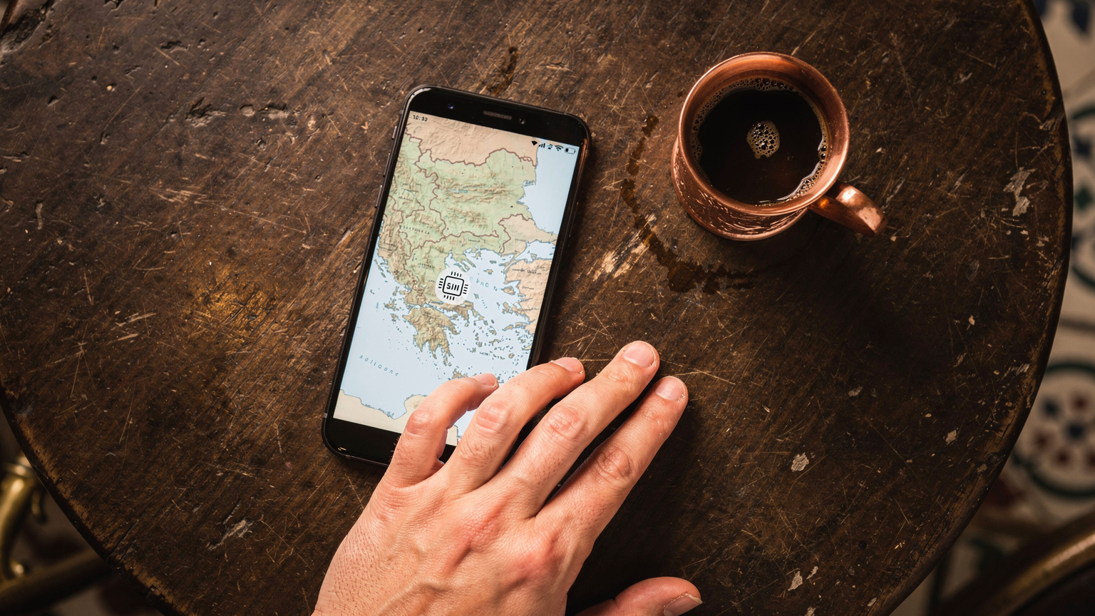 Eine Nahaufnahme zeigt ein Smartphone mit einem Balkan eSIM-Logo und einer Karte der Region, gehalten von einer Hand, die eine Tasse traditionellen türkischen Kaffees in Belgrad, Serbien, neben sich hat.
