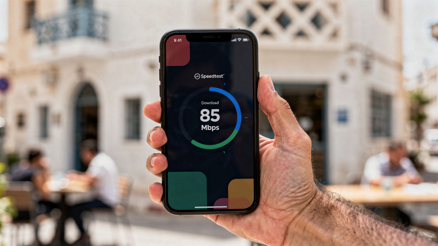 Un écran de smartphone affiche un test de vitesse réseau (Speedtest) avec un débit descendant de 85 Mbps, tenu par une main masculine dans le quartier de La Marsa à Tunis.