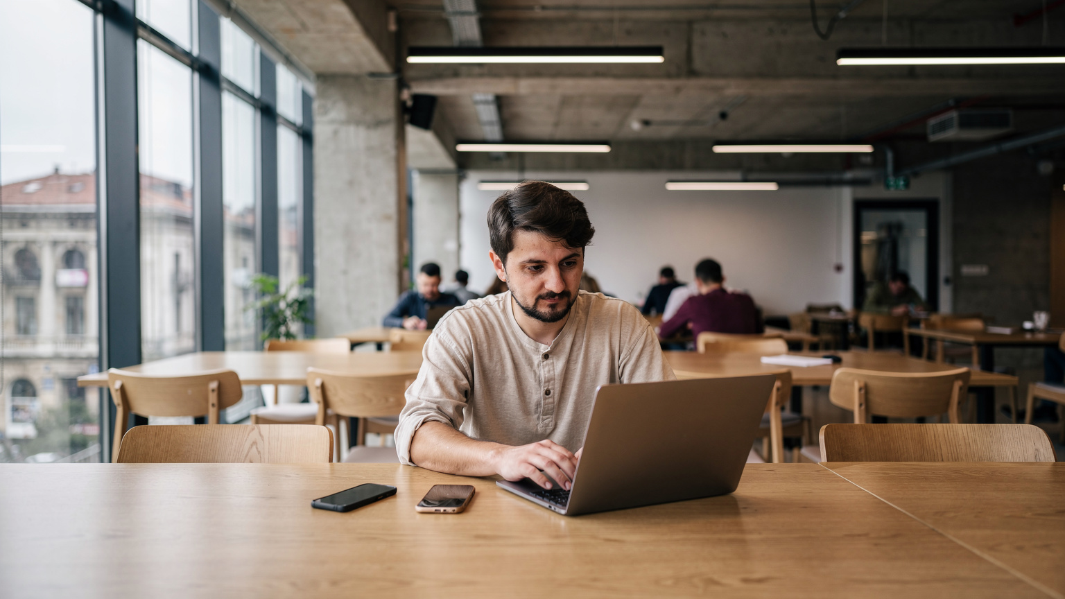 Ein Reisender arbeitet in einem modernen Co-Working-Space in Skopje, Nordmazedonien, mit seinem Laptop und einem Smartphone auf dem Tisch.