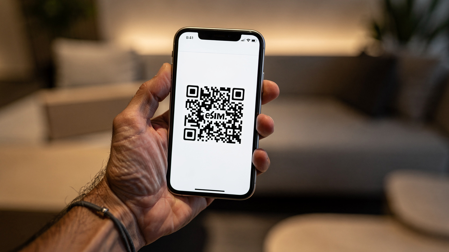 Nahaufnahme eines iPhone 11, das von einer Hand gehalten wird, während auf dem Bildschirm ein QR-Code für die eSIM-Installation angezeigt wird. Im Hintergrund ist eine unscharfe Hotellobby zu erkennen.
