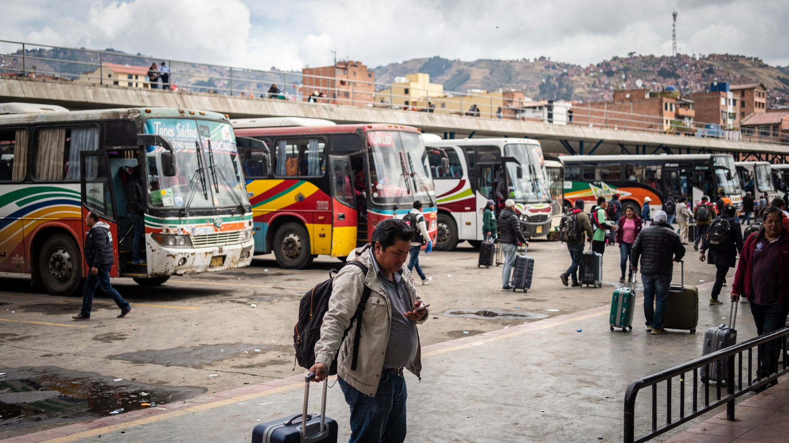 A wide shot of a bus station in La Paz, Bolivia, with various buses and people, focusing on the dynamic atmosphere of urban travel and connectivity challenges.
