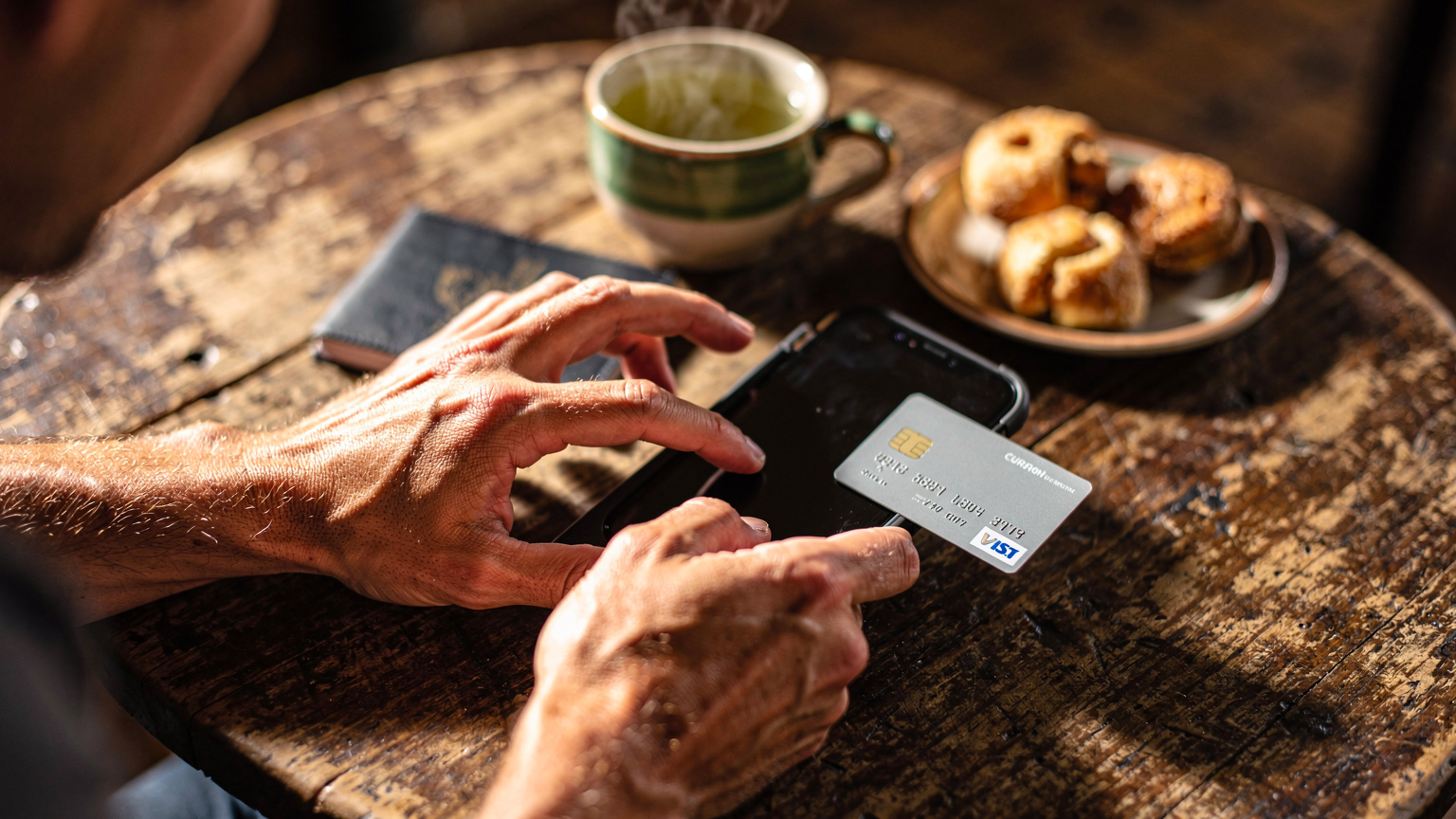 Manos de un viajero con pasaporte y una tarjeta de crédito en una mesa de un café en el barrio de San Blas en Cusco, Perú, intentando comprar una eSIM online.