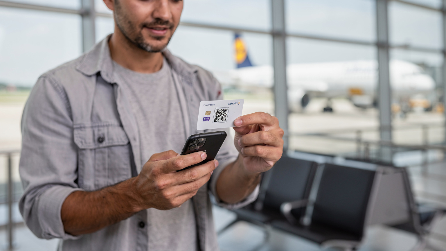 Ein Reisender am Münchner Flughafen Franz Josef Strauß scannt mit seinem iPhone 11 einen QR-Code zur eSIM-Aktivierung, um vor dem Abflug verbunden zu sein.