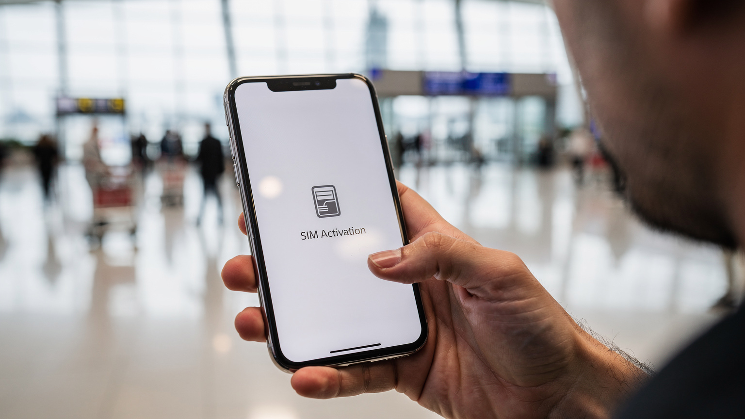 صورة مقربة لشاشة هاتف ذكي تعرض خيارات تفعيل شريحة eSIM، مع خلفية ضبابية لمطار إسطنبول الدولي المزدحم، يظهر فيها المسافرون وعربات الأمتعة.