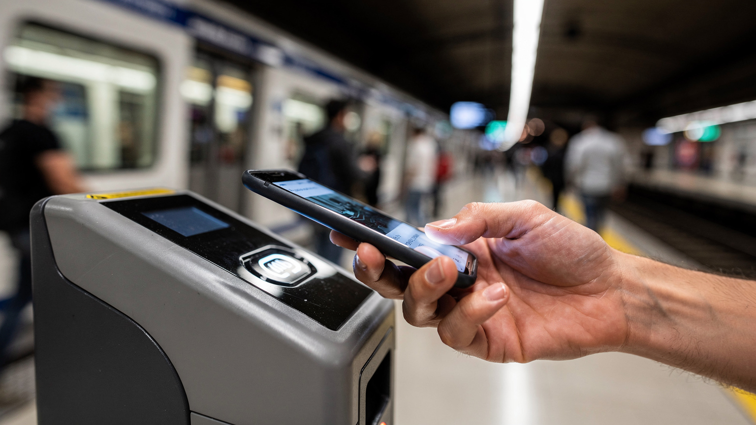Un primo piano di un terminale di pagamento contactless con una mano che tiene uno smartphone abilitato NFC, mentre persone passano rapidamente sullo sfondo di una stazione della metropolitana di Roma, illuminata da luci artificiali intense.