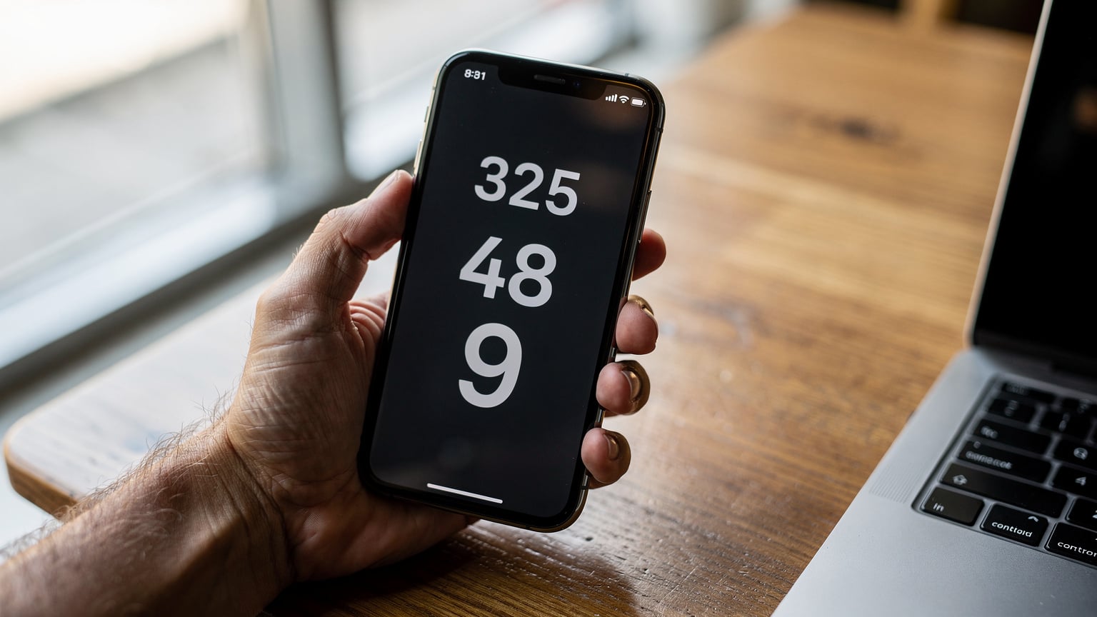 A close-up of a person's hand holding a smartphone, displaying the Ookla Speedtest app interface with download, upload, and ping results clearly visible against a slightly blurred background of a cafe table.