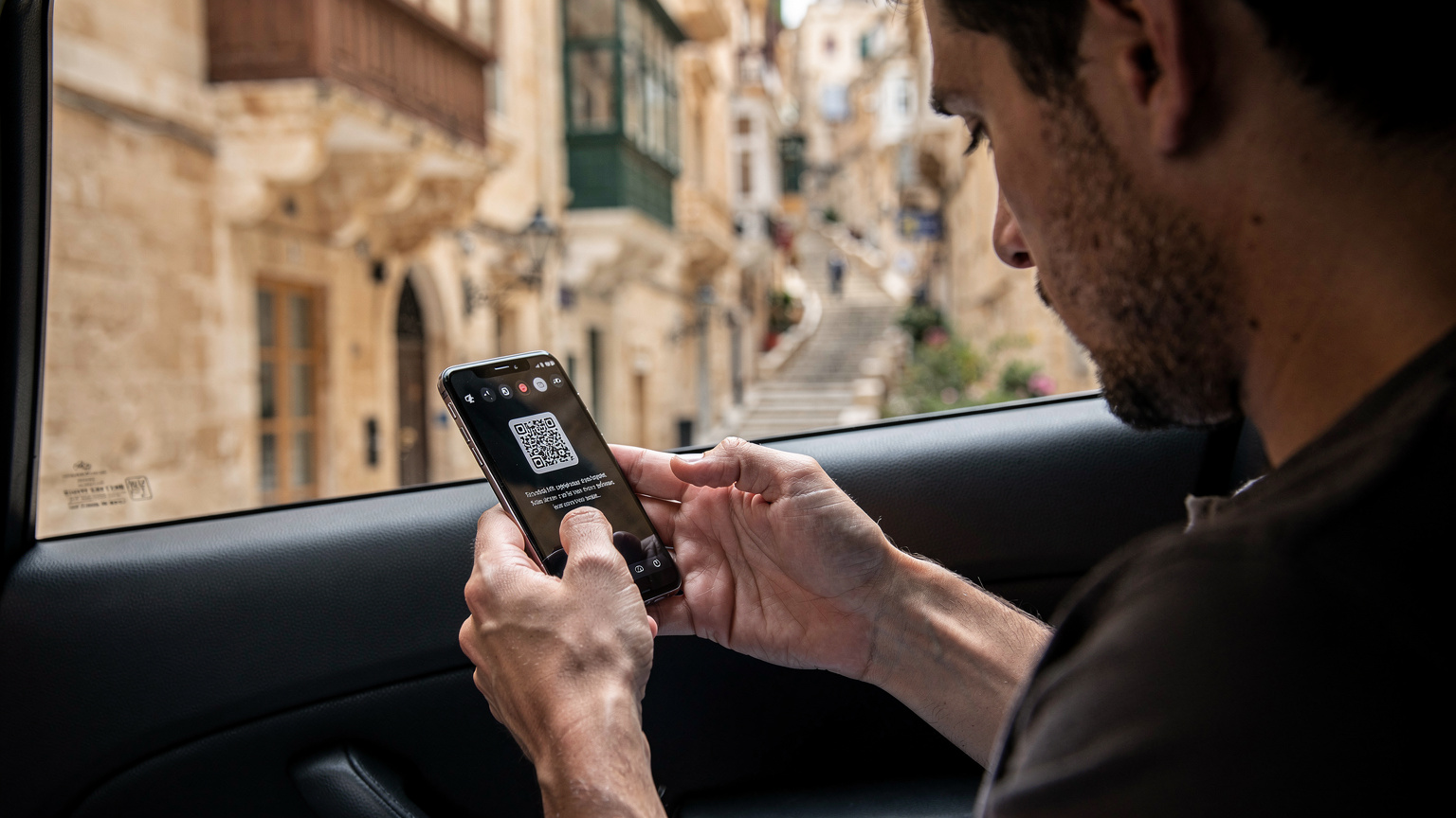 Un viaggiatore sta installando una eSIM sul suo smartphone mentre si trova all'interno di un taxi che attraversa le vie di La Valletta, Malta.