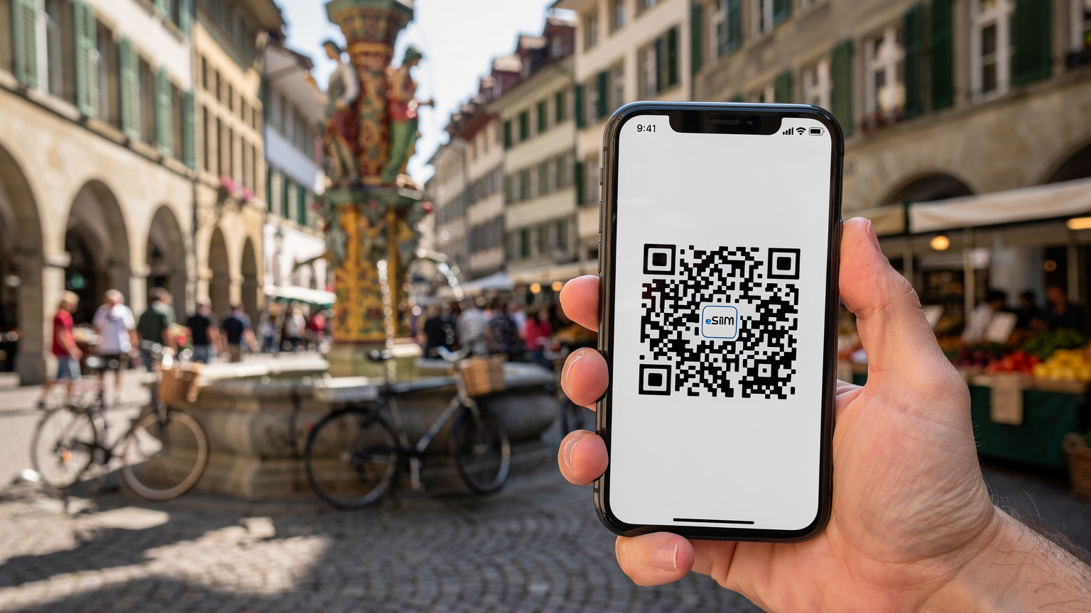 O persoană ține un smartphone care afișează un cod QR pentru activarea eSIM, în timp ce pe fundal se zărește o piață aglomerată din Vechiul Oraș din Berna, cu o fântână ornamentată.