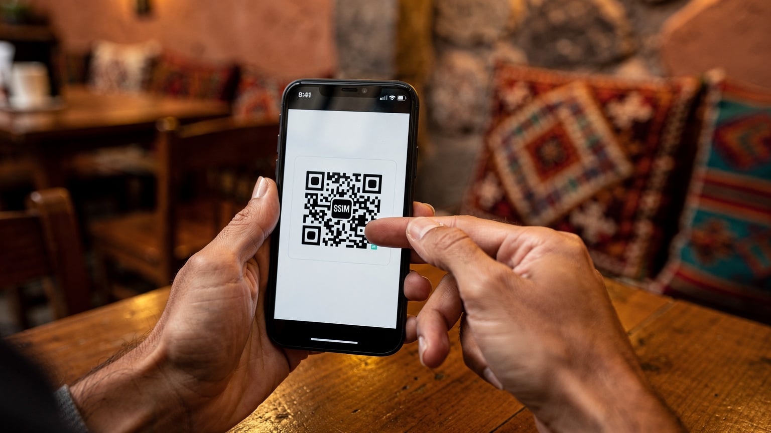 A close-up shot of hands holding a smartphone, displaying an eSIM activation QR code against a blurred background of a cozy cafe interior in Cusco, Peru.