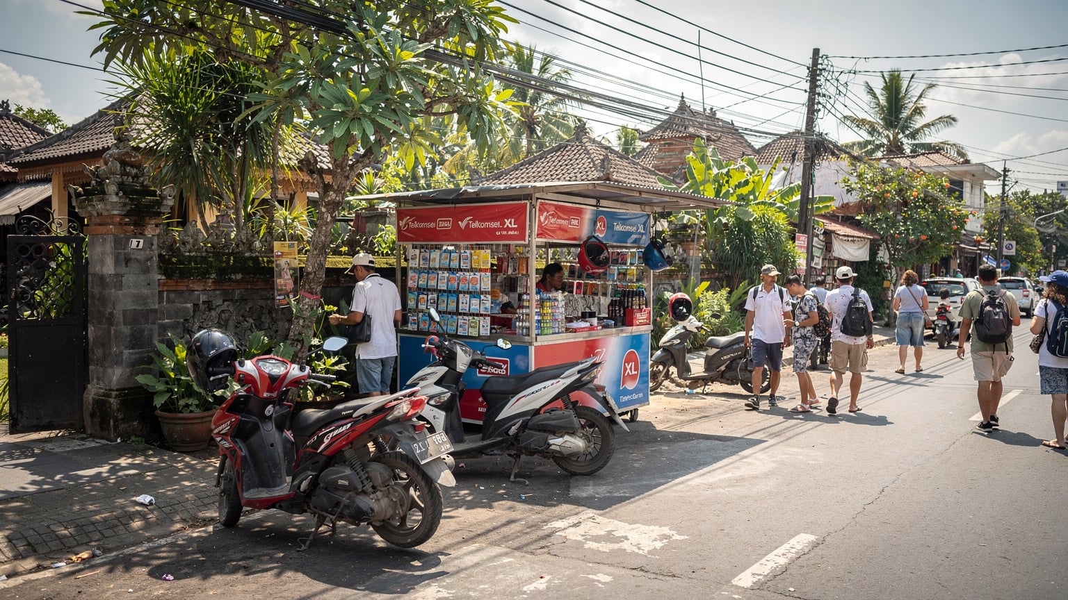 A vibrant street scene in Canggu, Bali, with a small roadside kiosk selling local SIM cards, motorcycles parked nearby, and people walking by under the tropical sun.