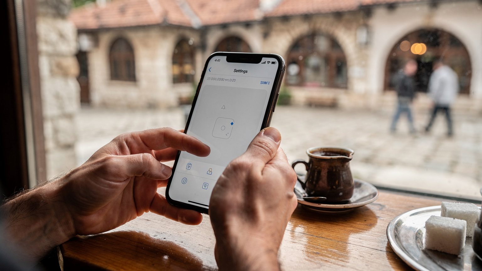 En kvinna tittar på sin iPhone för att installera ett eSIM vid ett kafébord i centrala Sarajevo, med traditionella byggnader i bakgrunden.